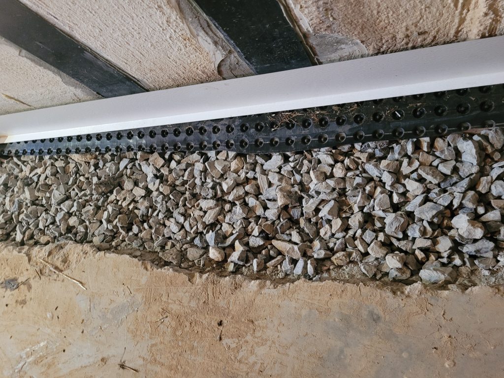 Interior drainage track installation for Basement Waterproofing in Roanoke, VA, showing washed stone and a sub-floor drainage system before concrete restoration.